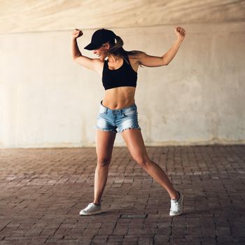 Strong willed and determined. Full length shot of an attractive young female street dancer flexing her biceps while practising out in the city.
