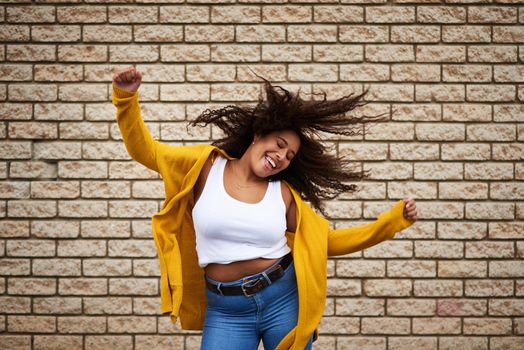 Be authentic and show off your moves. a happy young woman dancing against a brick wall.