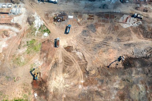 Aerial top view of excavators and dump trucks working at the construction site