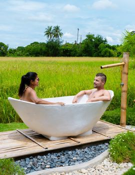 men and women in bath tub outside on vacation at a homestay in Thailand with green rice paddy field