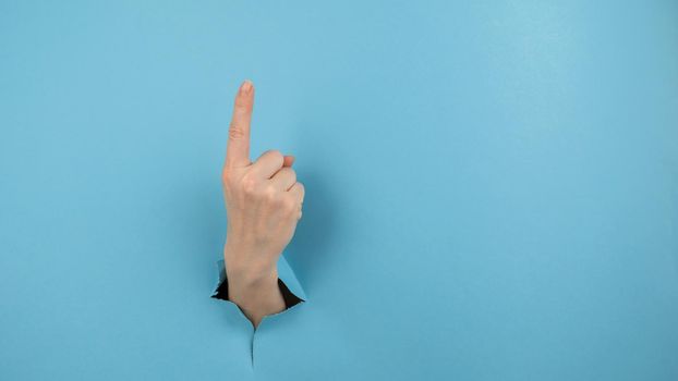 A woman's hand sticking out of a hole from a blue background shows her index finger up.