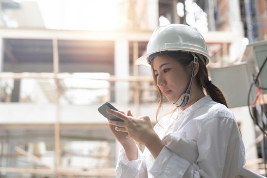 Asian construction workers using smartphone and holding blueprint at the construction site.