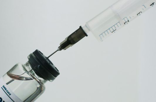 A vaccination syringe and a glass ampoule with a clear liquid.