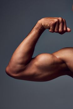 I worked too hard to get this. Studio shot of a muscular shirtless young sportsman flexing his bicep against a grey background.