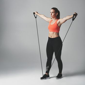 Resistance training is good for the whole body. Studio shot of an athletic young woman working out with a resistance band against a grey background