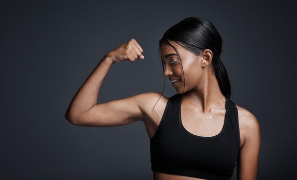 Once you see results, it becomes an addiction. Studio shot of a young sportswoman flexing her bicep against a gray background.