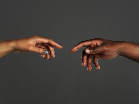 In touching distance. Studio shot of two unrecognizable people reaching out their hands towards each other against a grey background.