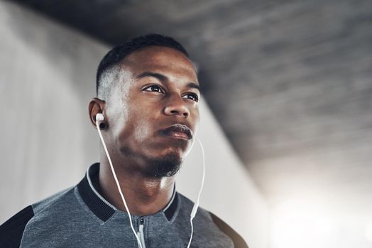 The music is all the motivation he needs. a handsome young man listening to music while exercising outside.