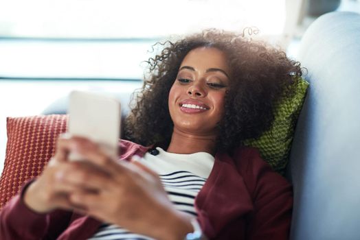 Connect and catch up with all of your favourites. a young woman using a mobile phone while relaxing on the sofa at home.