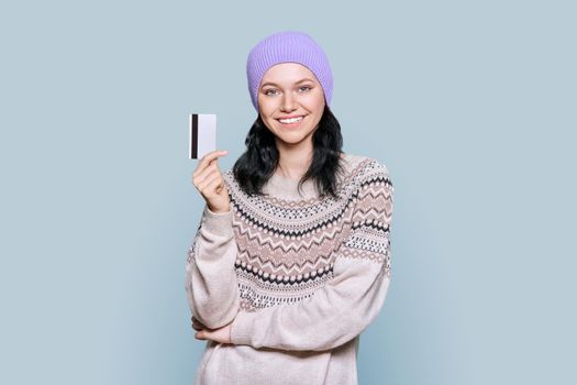 Young beautiful teenage female with credit card on light gray background