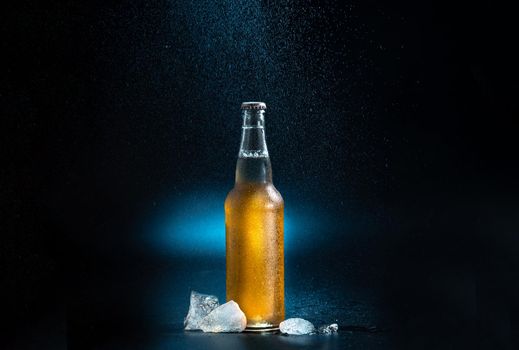 amber beer bottle, splashing drops on a black and blue background. A beer bottle with splashing drops with ice chunks on a dark background
