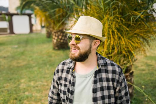 Laughing attractive man wearing hat over palm tree background with copy space - emotion and vacation travel holidays concept