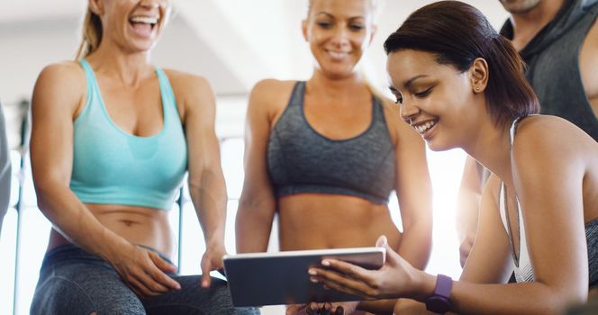 Nothing like a little muscle motivation courtesy of the internet. a group of happy young women using a digital tablet together in a gym.