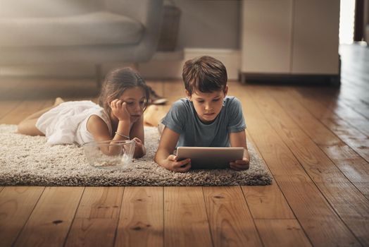 Curious about the world that connects us. an adorable brother and sister using a digital tablet together on the floor at home.