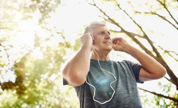 Healthy, fit and active senior man listening to music while running, exercising and training outside from below. Happy, sporty and real mature male doing a cardio and endurance workout outdoors