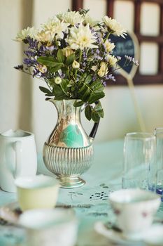 What is a classy party without a vase of flowers. a metal vase filled with flowers on a table at a tea party inside.