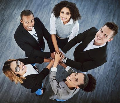 We always aim high. High angle shot of a group of businesspeople joining their hands together in a huddle.