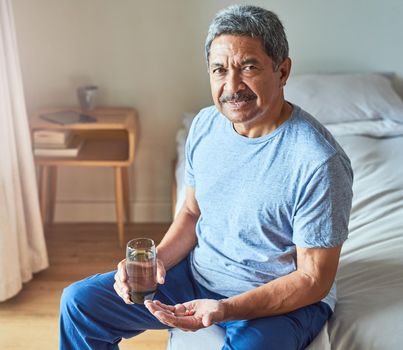 I hate taking medication this early in the morning. Portrait of a cheerful mature man seated on his bed and about to drink medication with water in the bedroom at home during the day.