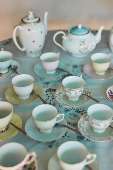 The table is set, time to begin the tea party. tea pots and tea cups laid out on a table at a tea party inside.