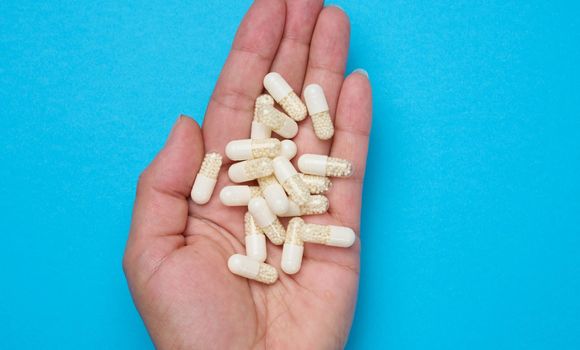 Woman's hand holding white oval pills on blue background
