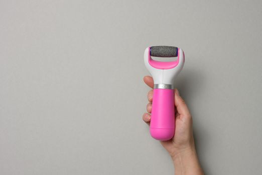 Woman's hand holding an electric pedicure tool on a gray background