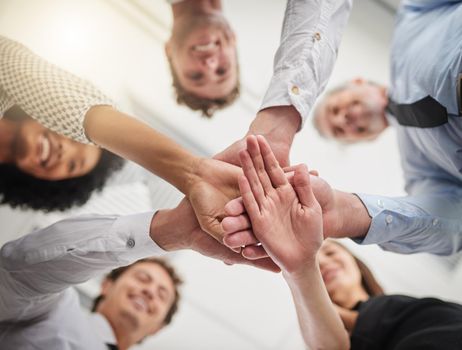 Success is the hands of a team. Low angle shot of a group of colleagues joining hands in solidarity in a modern office.