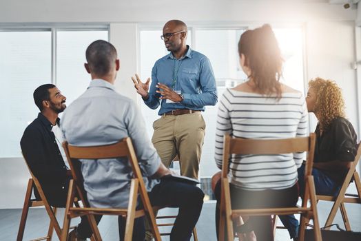 Leader, manager or boss talking to and teaching his team of employees and colleagues in a meeting, seminar or workshop at the office. Male CEO planning, discussing strategy and coaching staff at work