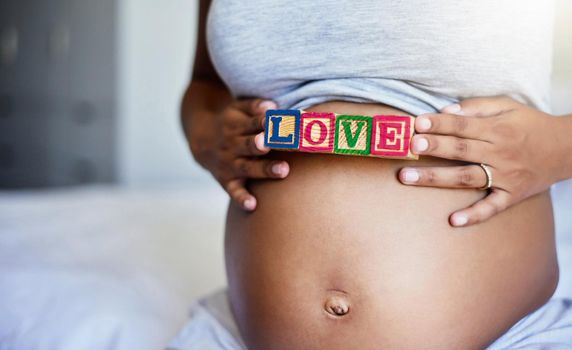 Made with love. a pregnant woman with wooden blocks on her belly that spell the word love.