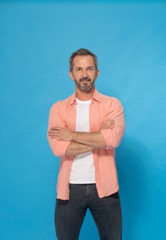 Strong handsome middle aged man with grey beard 40s, 50s wearing casual isolated on blue background. Smiling mature muscular, fit man posing in studio. Mature fit man health and physics