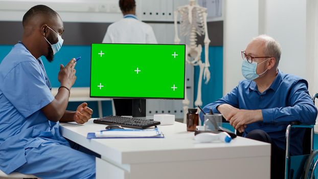 Specialist and old man looking at monitor with greenscreen