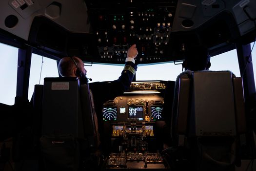 Male captain pushing dashboard buttons in plane cockpit