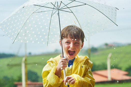Rainy season is his most favorite season. Portrait of a cheerful little boy standing with an umbrella outside on a rainy day.