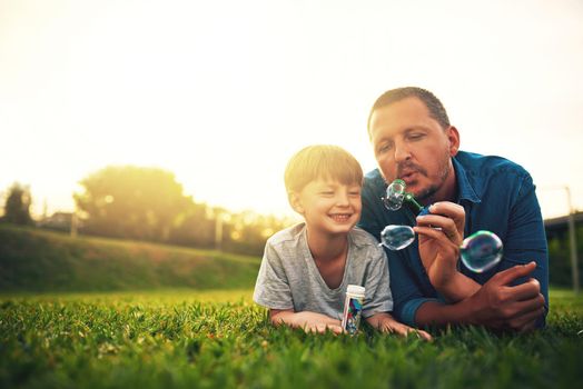 Blowing bubbles in the backyard is my favourite. a father and his adorable son blowing bubbles in the backyard.