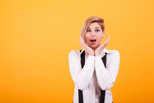 Attractive woman with blond hair looking shocked at camera over yellow background.