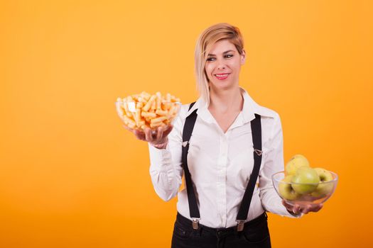 Beautiful blond woman with short hair balancing two bowls over yellow background.