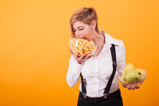 Pretty blond woman with short hair taking a bite from her corn puffs over yellow background.