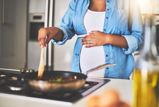 Cooking right up until her last trimester. a pregnant woman preparing a meal on the stove at home.