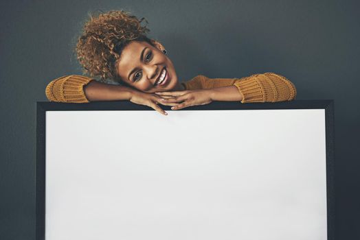 Woman standing with blank sign or portrait frame, showing copy space for advertising or marketing on dark background. Happy, smiling and relaxed Afro female portrait with big white poster copyspace