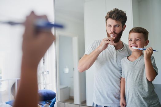 Giving their teeth a good clean. a father and his little son brushing their teeth together in the bathroom at home.