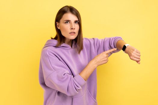 Woman with dark hair pointing wrist watch and looking annoyed displeased, showing clock to hurry up.