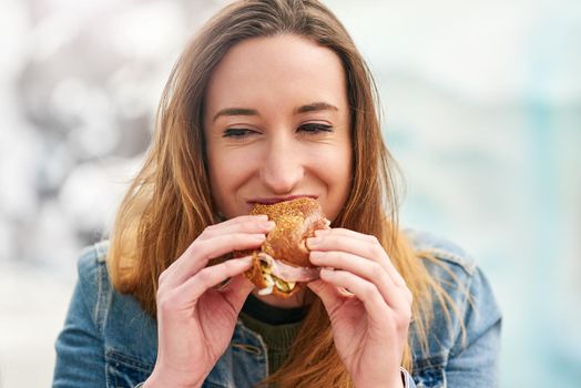 Quick snack then back to the fun. Portrait of a beautiful young woman eating a sandwich at an amusement park outside.