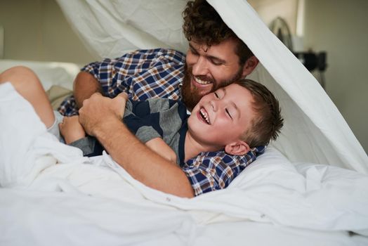 Here comes the tickle monster. a handsome young man and his son playing on the bed at home.