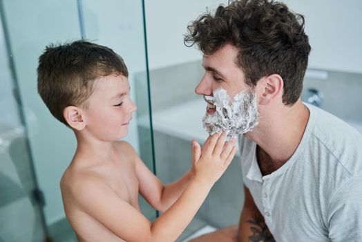 Your beard is so prickly Dad. a little boy rubbing shaving cream on his fathers face in the bathroom at home.