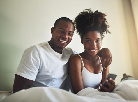 We never start the day without each other. Portrait of a happy young couple using a mobile phone together in bed at home.