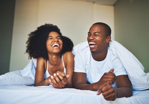 Laughter turns a good morning into a great morning. a happy young couple relaxing under a duvet in their bedroom.