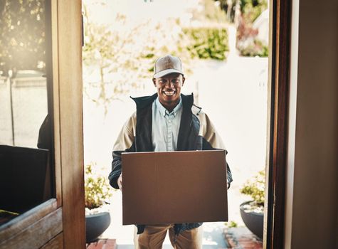 I have a delivery for you sir. Portrait of a cheerful young deliveryman holding a box while standing in a doorway at a house during the day.