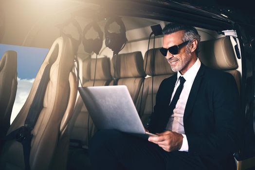 Success is in the air. a mature businessman using a laptop while traveling in a helicopter.
