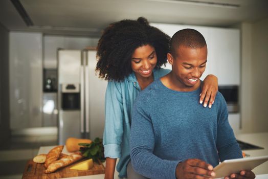What are you up to. a cheerful young couple relaxing in the kitchen while browsing on a digital tablet at home during the day.
