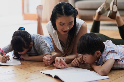 Teaching the kids how homework is done. a cheerful mother and her two children doing homework together while lying on the floor at home during the day.