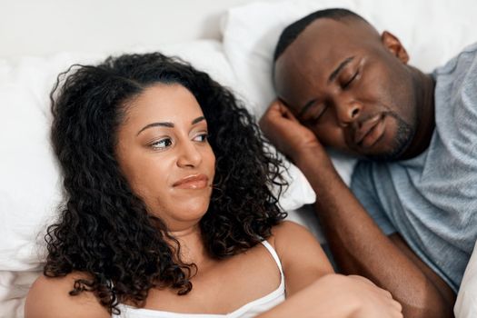 I cant sleep with this noise. a irritated looking young woman lying in bed with her husband and trying to get some sleep but cant due to his snoring.